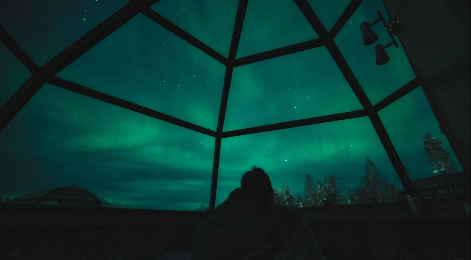 Northern Lights glowing green through the glass roof of a Rovaniemi igloo