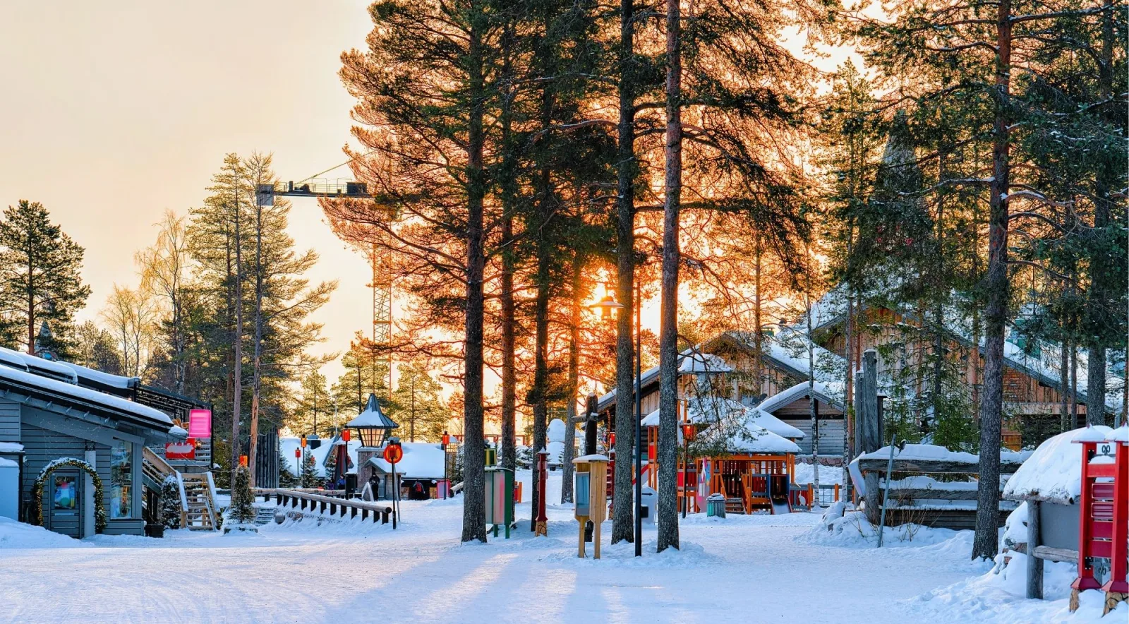 Golden winter sunset over the wooden buildings and pines of Santa Claus Village