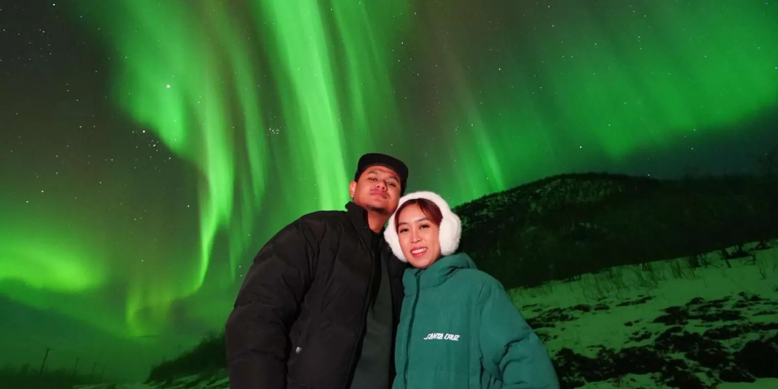 Couple smiling beneath a vivid green aurora on a Rovaniemi Northern Lights tour