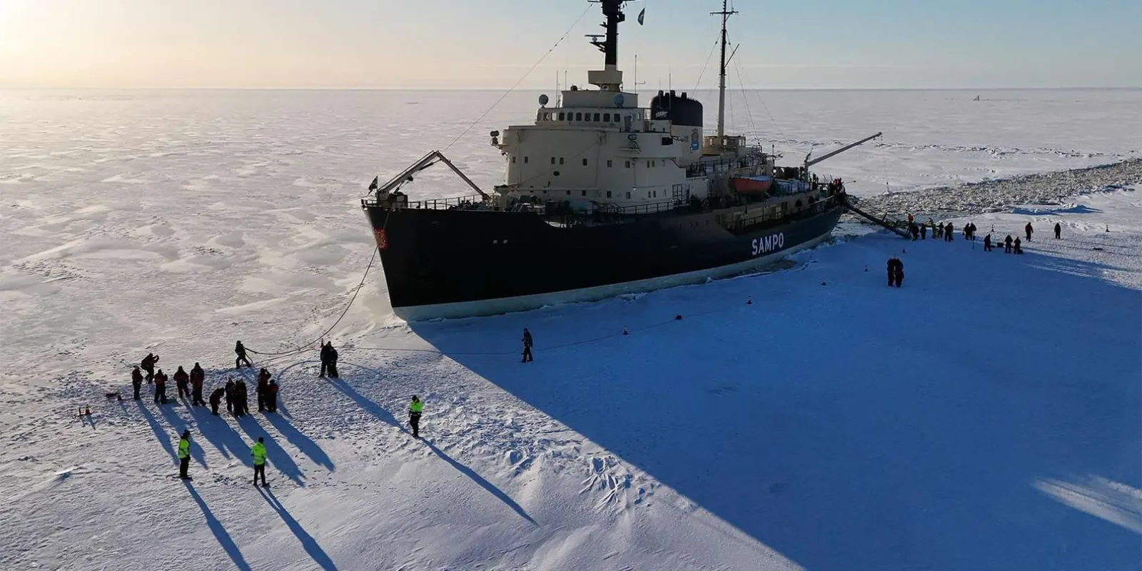 Travelers walking on the frozen sea beside the Sampo icebreaker